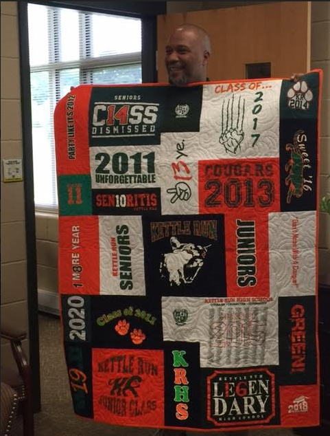Former principal Major Warner holds up a gift from Lisa Heckathorn: a quilt featuring
all the class logos from the ten years he had served as principal