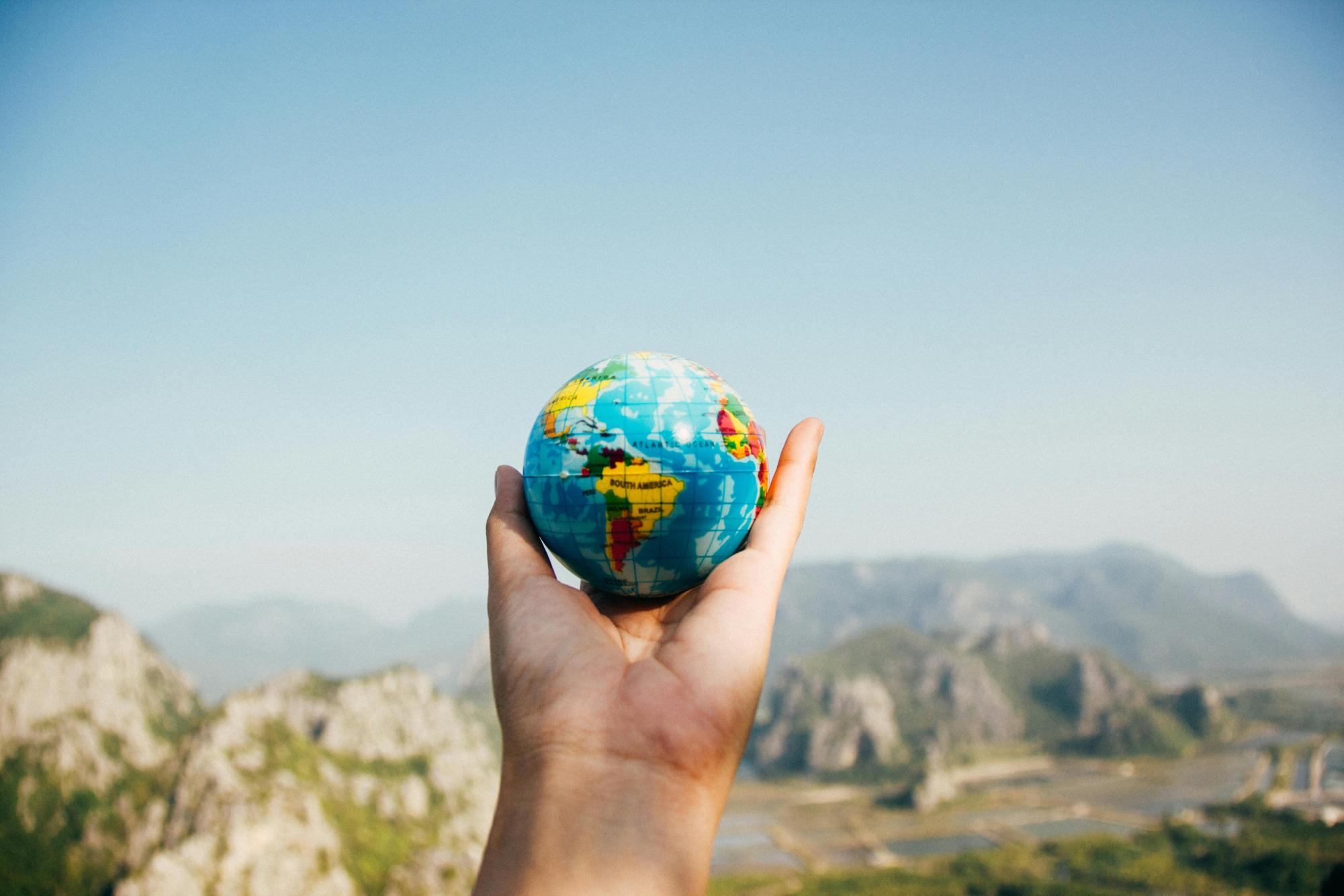 Person Holding World Globe Facing Mountain
